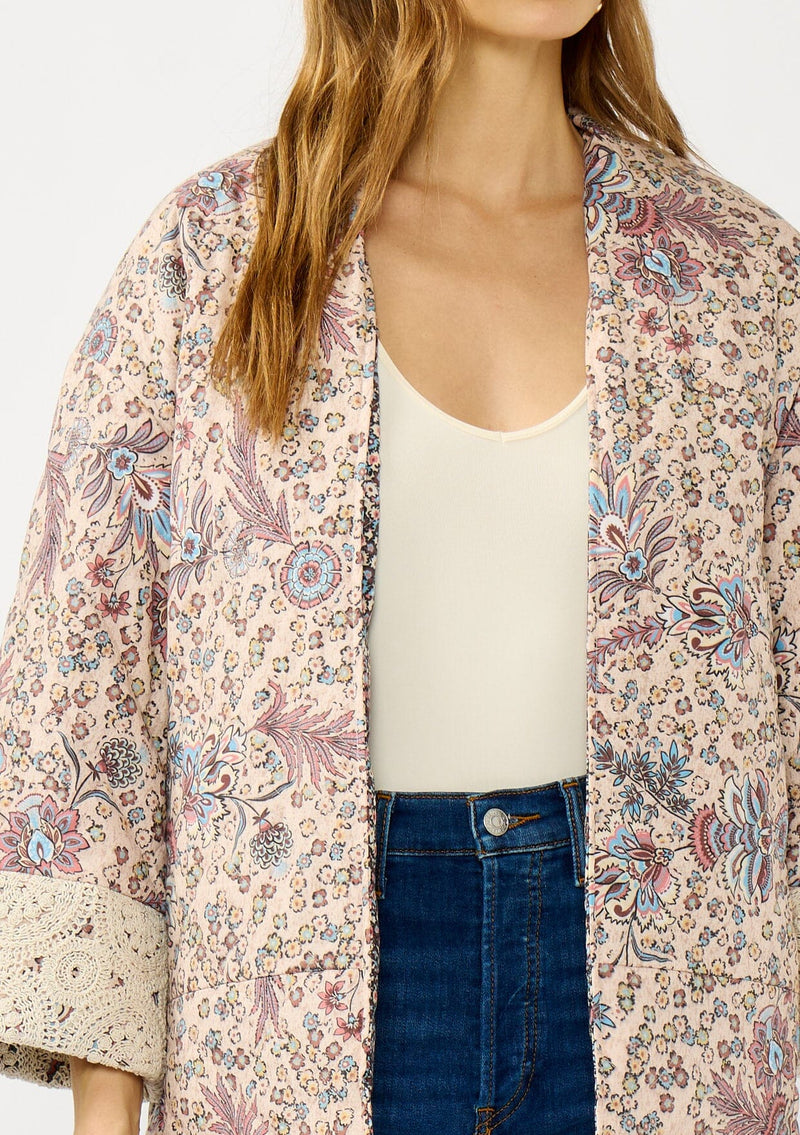 [Color: Mauve/Natural] A detail  image of a blonde model wearing a mauve pink floral bohemian jacket with an oversized fit, long sleeves, crochet trim, and side pockets. 