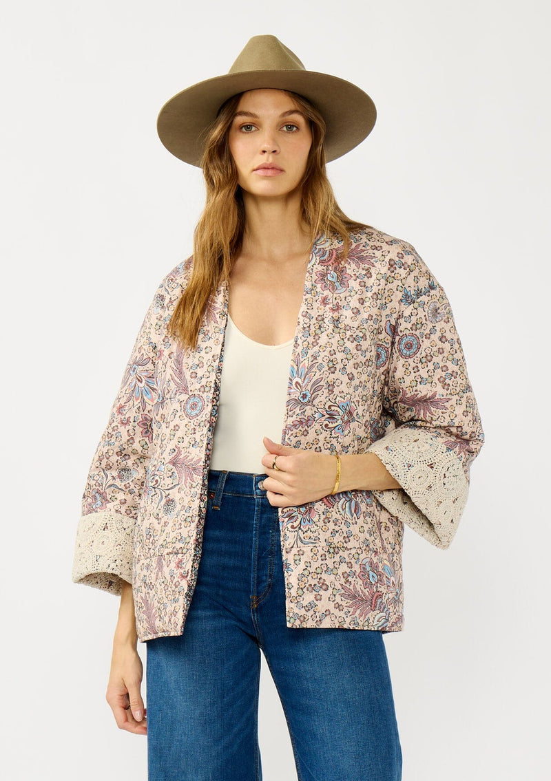 [Color: Mauve/Natural] A front facing image of a blonde model wearing a mauve pink floral bohemian jacket with an oversized fit, long sleeves, crochet trim, and side pockets. 