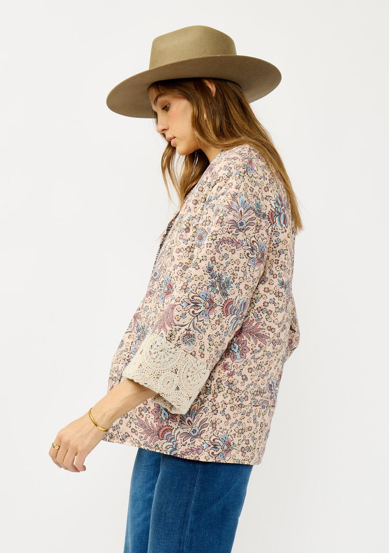 [Color: Mauve/Natural] A side facing image of a blonde model wearing a mauve pink floral bohemian jacket with an oversized fit, long sleeves, crochet trim, and side pockets. 