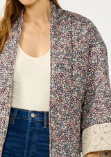 [Color: Mauve/Natural] A detail image of a blonde model wearing a reversible mauve pink floral bohemian jacket with an oversized fit, long sleeves, crochet trim, and side pockets. 