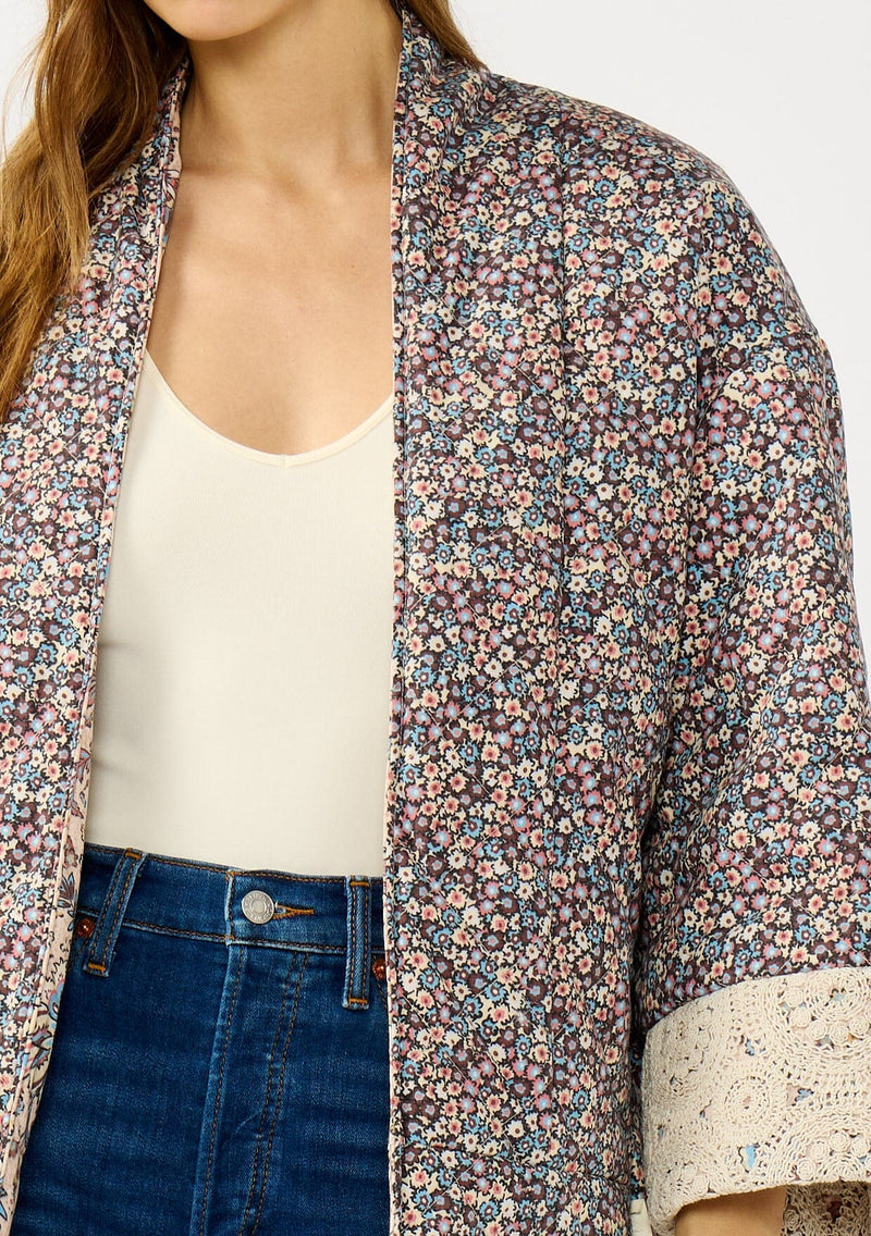[Color: Mauve/Natural] A detail image of a blonde model wearing a reversible mauve pink floral bohemian jacket with an oversized fit, long sleeves, crochet trim, and side pockets. 