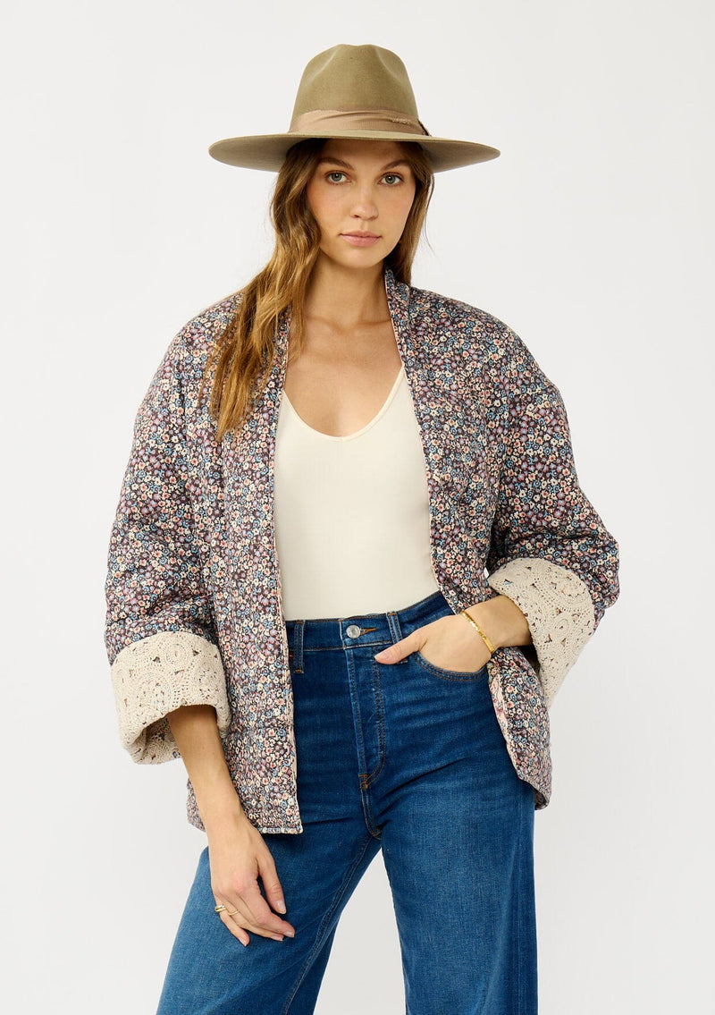 [Color: Mauve/Natural] A front facing image of a blonde model wearing a mauve pink floral bohemian jacket with an oversized fit, long sleeves, crochet trim, and side pockets. 