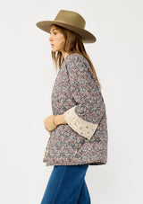 [Color: Mauve/Natural] A side facing image of a blonde model wearing a reversible mauve pink floral bohemian jacket with an oversized fit, long sleeves, crochet trim, and side pockets. 