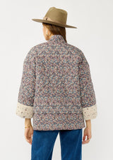 [Color: Mauve/Natural] A back facing image of a blonde model wearing a reversible mauve pink floral bohemian jacket with an oversized fit, long sleeves, crochet trim, and side pockets. 