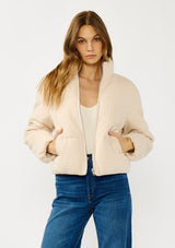 [Color: Natural] A front facing image of a blonde model wearing a light beige soft knit puffer jacket with a zipper front, high collar, and side pockets. A classic fall jacket for cold weather. 