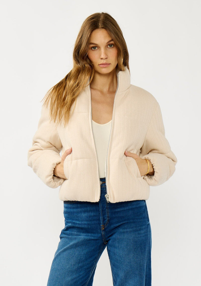 [Color: Natural] A front facing image of a blonde model wearing a light beige soft knit puffer jacket with a zipper front, high collar, and side pockets. A classic fall jacket for cold weather. 