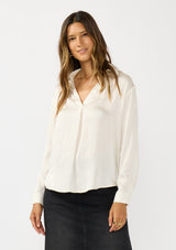 [Color: Eggshell] A front facing image of a brunette model wearing an ivory silky poly satin blouse with a split v-neckline, collar, and long sleeves with button cuffs. 