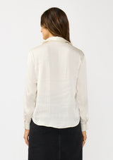 [Color: Eggshell] A back facing image of a brunette model wearing an ivory silky poly satin blouse with a split v-neckline, collar, and long sleeves with button cuffs. 