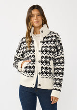 [Color: Cream/Black] A front facing image of a brunette model wearing a black and cream button front knit sweater with a high neckline and side pockets. A cold weather layering piece for the fall and winter season. 