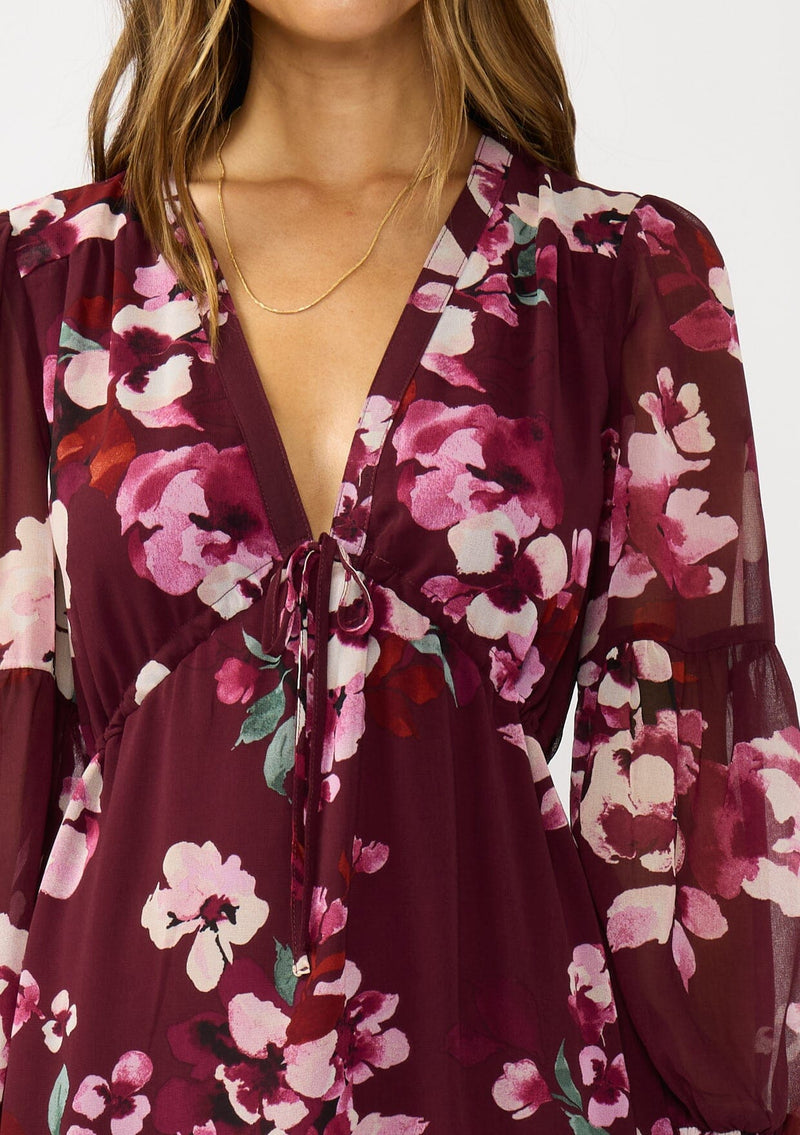 [Color: Wine/Dusty Rose] A detail image of a brunette model wearing a burgundy floral maxi dress with an empire waist with drawstring, long sleeves, and a deep v-neckline. An elegant dress for the holidays or other special occasions. 