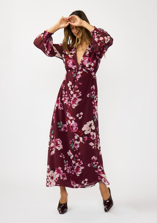 [Color: Wine/Dusty Rose] A front facing image of a brunette model wearing a burgundy floral maxi dress with an empire waist with drawstring, long sleeves, and a deep v-neckline. An elegant dress for the holidays or other special occasions. 