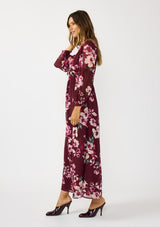 [Color: Wine/Dusty Rose] A side facing image of a brunette model wearing a burgundy floral maxi dress with an empire waist with drawstring, long sleeves, and a deep v-neckline. An elegant dress for the holidays or other special occasions. 