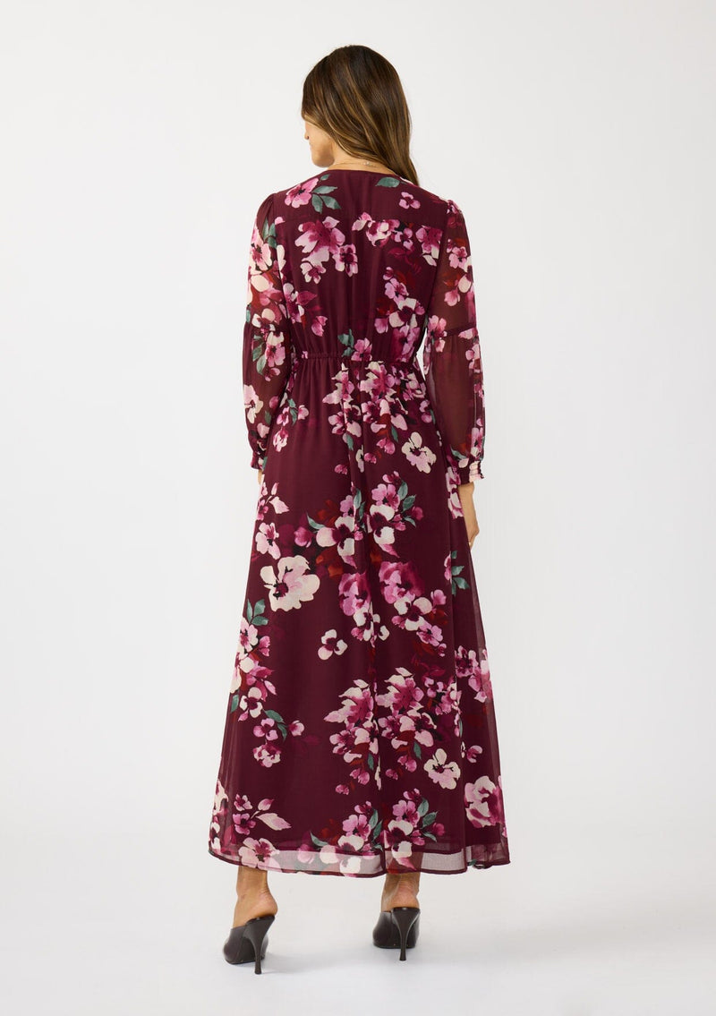 [Color: Wine/Dusty Rose] A back facing image of a brunette model wearing a burgundy floral maxi dress with an empire waist with drawstring, long sleeves, and a deep v-neckline. An elegant dress for the holidays or other special occasions. 