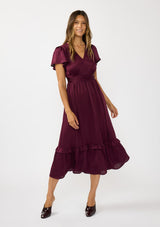 [Color: Merlot] A front facing image of a brunette model wearing a burgundy holiday midi dress with a short flutter sleeves, a defined waistline with gathered fabric, and a ruffled tiered skirt. Elegant and formal for date nights, holiday parties, and other special occasions. 
