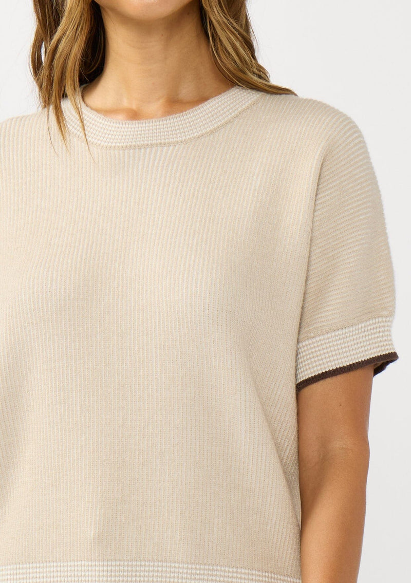 [Color: Heather Stone/Natural] A detail image of a brunette model wearing a tan cozy knit short sleeve sweater top with a round neckline and contrast ribbed trims. 