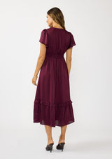 [Color: Merlot] A back facing image of a brunette model wearing a burgundy holiday midi dress with a short flutter sleeves, a defined waistline with gathered fabric, and a ruffled tiered skirt. Elegant and formal for date nights, holiday parties, and other special occasions. 