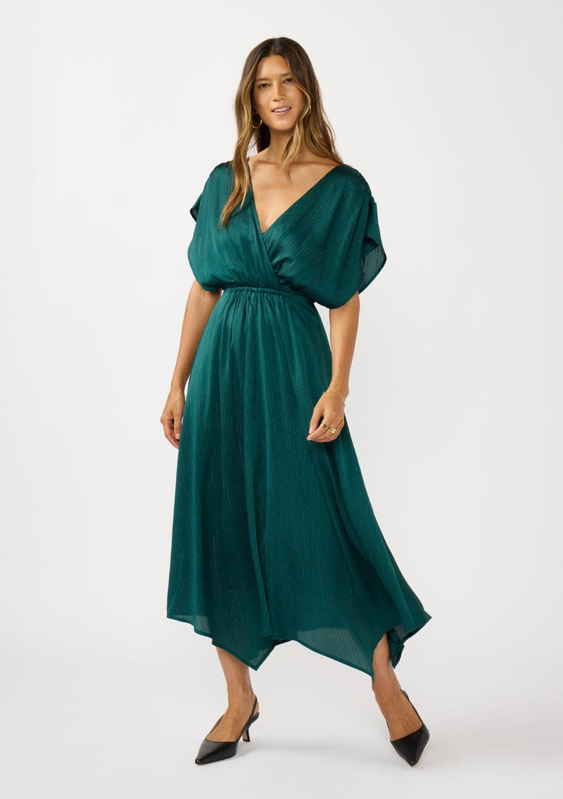 [Color: Emerald] A front facing image of a brunette model wearing a formal holiday party dress with sparkly metallic stripe details. Featuring a surplice v-neckline, short dolman sleeves, an elastic waist, and an asymmetrical hemline. 