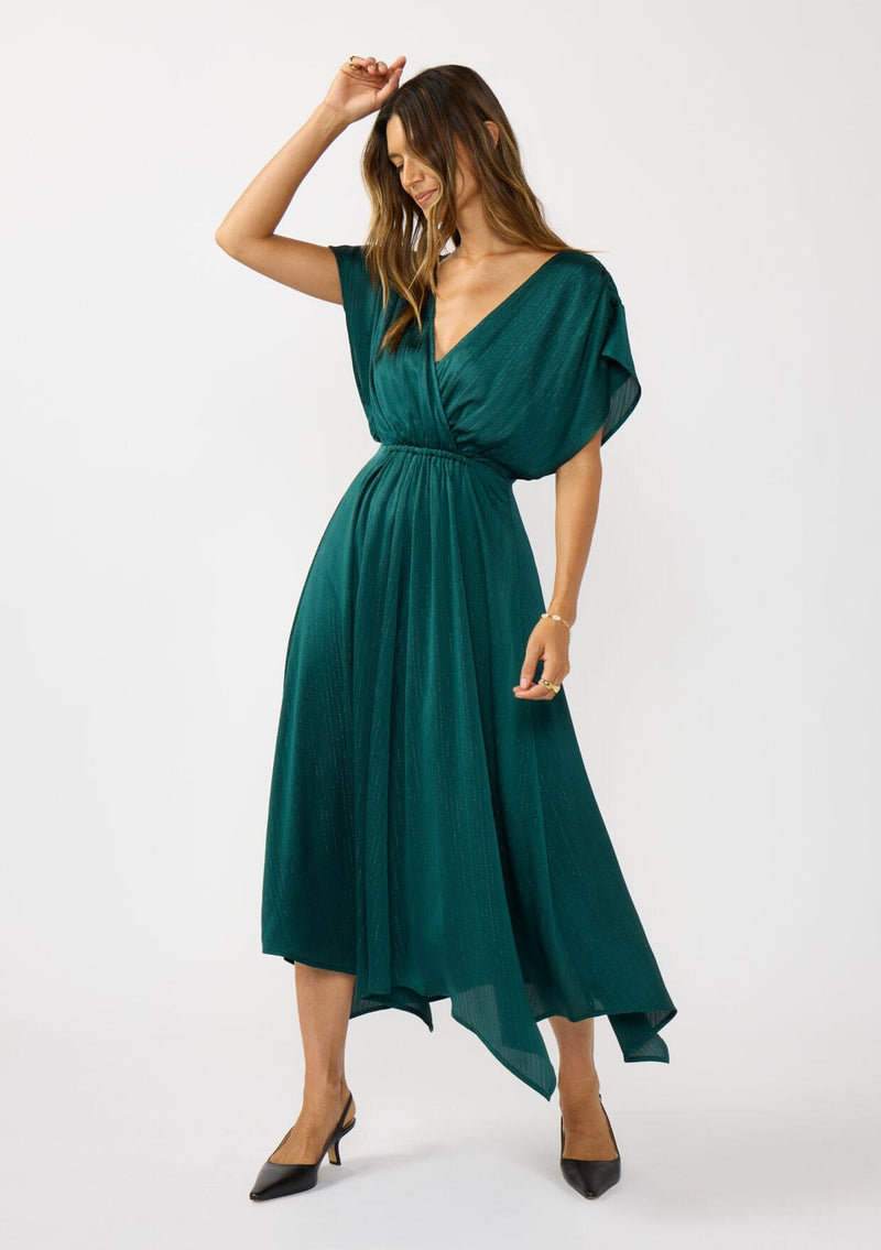 [Color: Emerald] A front facing image of a brunette model wearing a formal holiday party dress with sparkly metallic stripe details. Featuring a surplice v-neckline, short dolman sleeves, an elastic waist, and an asymmetrical hemline. 
