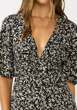 [Color: Black/Natural] A detail image of a brunette model wearing a black and white abstract maxi dress with a deep v-neckline, half sleeves, empire waist, and a sexy side slit.