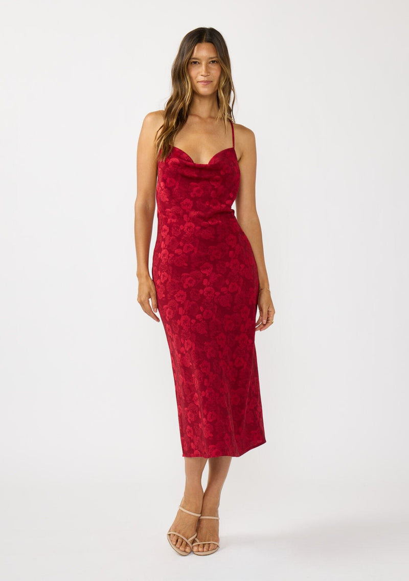 [Color: Red] A front facing image of a brunette model wearing a holiday floral jacquard midi dress with a cowl neckline, adjustable straps, and a cross back. Elegant and timeless for holiday parties, weddings, and other special occasions. 