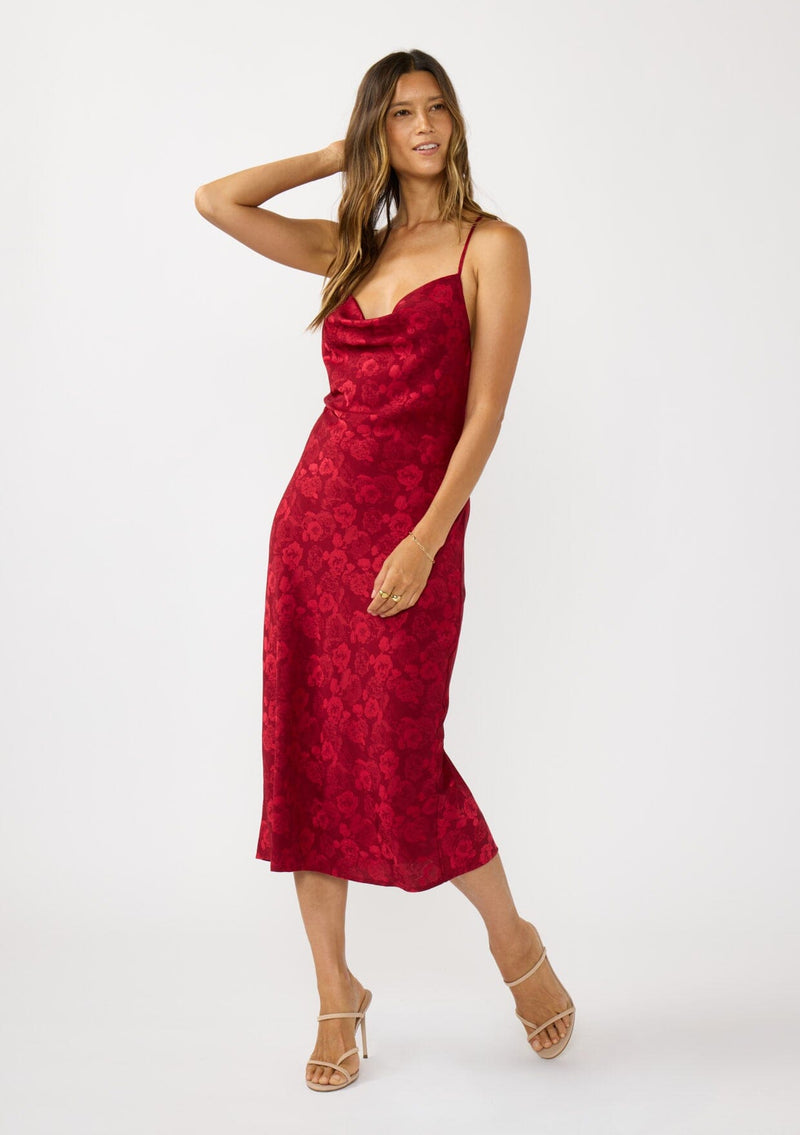 [Color: Red] A front facing image of a brunette model wearing a holiday floral jacquard midi dress with a cowl neckline, adjustable straps, and a cross back. Elegant and timeless for holiday parties, weddings, and other special occasions. 