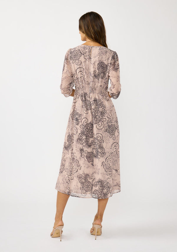 [Color: Natural/Brown] A back facing image of a brunette model wearing a nude brown floral midi dress with a v-neckline, 3/4 length sleeves, and a flattering empire waist. 