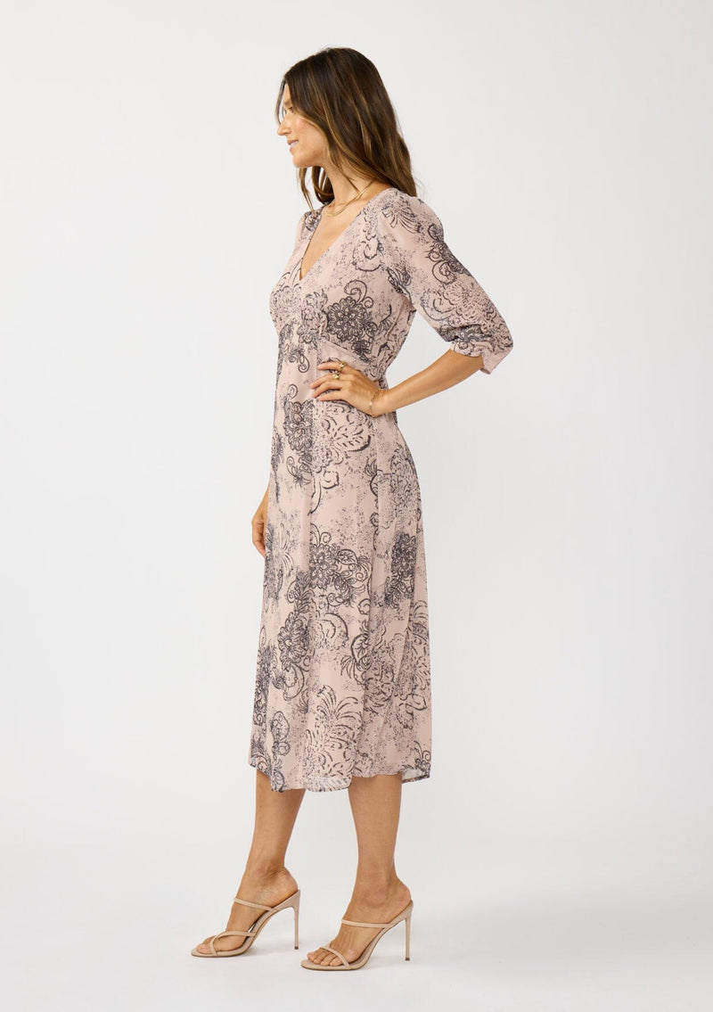 [Color: Natural/Brown] A side facing image of a brunette model wearing a nude brown floral midi dress with a v-neckline, 3/4 length sleeves, and a flattering empire waist. 