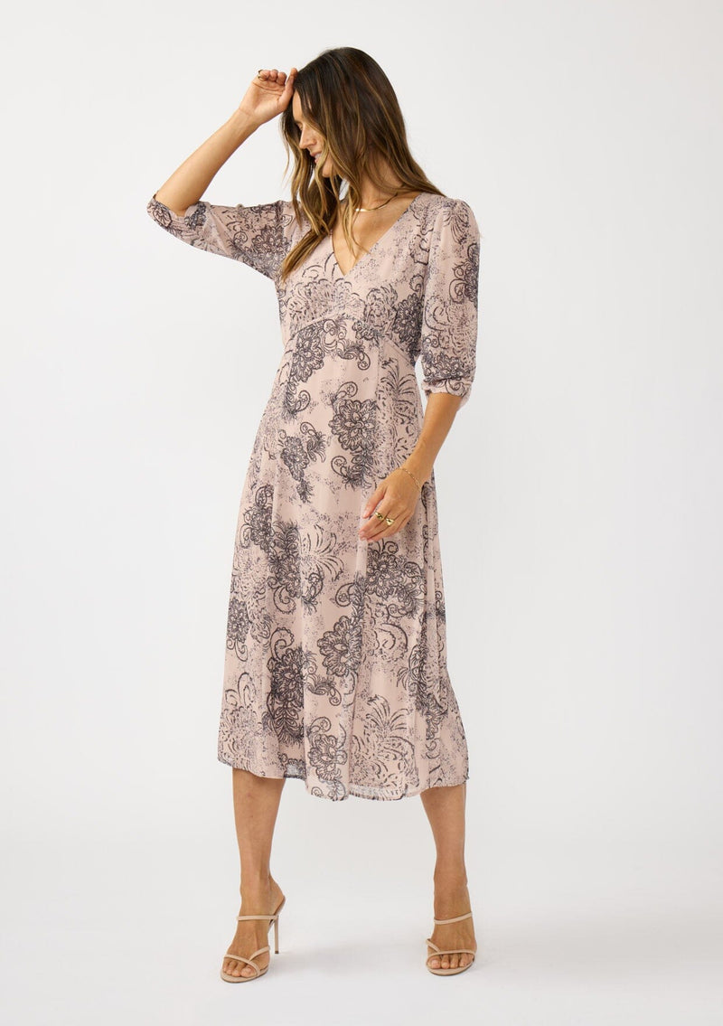[Color: Natural/Brown] A front facing image of a brunette model wearing a nude brown floral midi dress with a v-neckline, 3/4 length sleeves, and a flattering empire waist. 