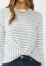 [Color: Ivory/Dusty Blue] A detail image of a brunette model wearing a classic ivory and light blue striped knit pullover sweater. With long sleeves, a drop shoulder, a crew neckline, and a twist front detail at the waist. 