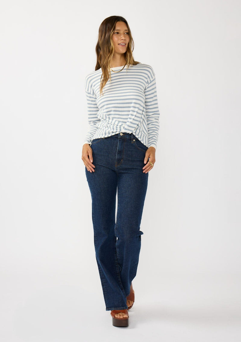 [Color: Ivory/Dusty Blue] A front facing image of a brunette model wearing a classic ivory and light blue striped knit pullover sweater. With long sleeves, a drop shoulder, a crew neckline, and a twist front detail at the waist. 