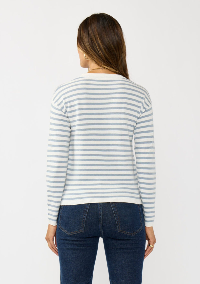 [Color: Ivory/Dusty Blue] A back facing image of a brunette model wearing a classic ivory and light blue striped knit pullover sweater. With long sleeves, a drop shoulder, a crew neckline, and a twist front detail at the waist. 