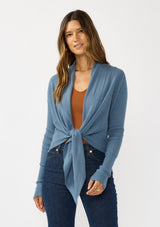 [Color: Heather Ocean] A photo of a Lovestitch model wearing a chic blue waffle knit wrap front sweater with long sleeves, a v neckline, and a button closure at the back. The long ties can be styled in multiple ways.