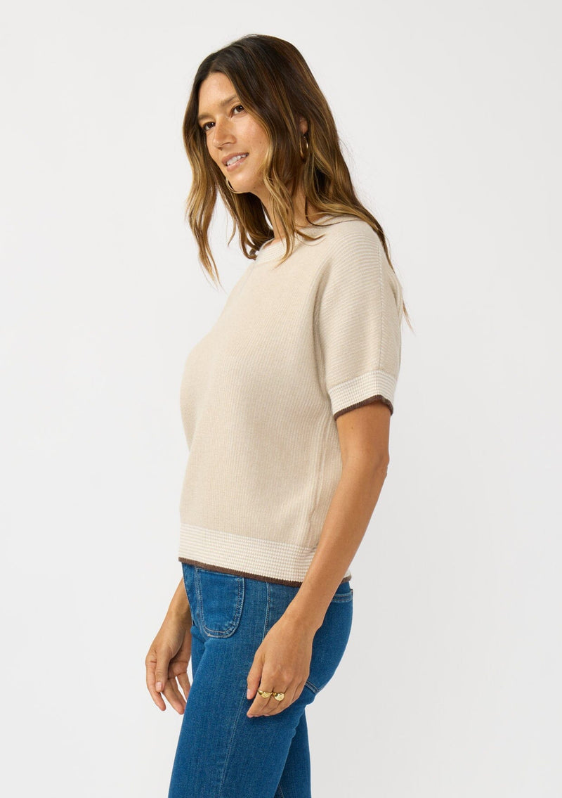 [Color: Heather Stone/Natural] A side facing image of a brunette model wearing a tan cozy knit short sleeve sweater top with a round neckline and contrast ribbed trims. 