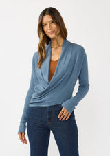 [Color: Heather Ocean] A photo of a Lovestitch model wearing a chic blue waffle knit wrap front sweater with long sleeves, a v neckline, and a button closure at the back. The long ties can be styled in multiple ways.