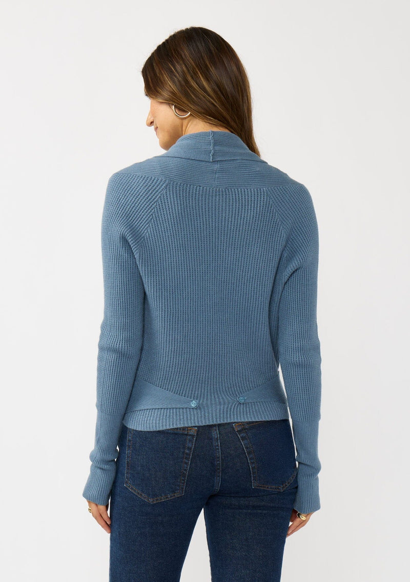 [Color: Heather Ocean] A photo of a Lovestitch model wearing a chic blue waffle knit wrap front sweater with long sleeves, a v neckline, and a button closure at the back. The long ties can be styled in multiple ways.