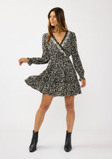 [Color: Black/Taupe] A front facing image of a brunette model wearing an abstract ivory and black mini dress with embroidered top. Featuring long sleeves, elastic ruffled cuffs, a surplice v-neckline, elastic waist, and a ruffle trimmed tiered hem. 