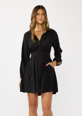 [Color: Black] A front facing image of a brunette model wearing a black dress with embroidered sleeves, a button front, a collared v-neckline, and side pockets. Effortlessly boho and casual for day to night. 