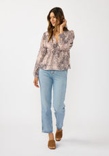 [Color: Natural/Brown] A front facing image of a brunette model wearing a nude brown floral blouse with a deep v-neckline, and ruffle accents on the front and sleeves. A classic boho top for casual outings and special occasions.  