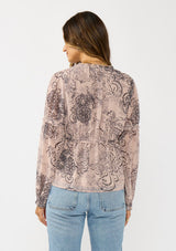 [Color: Natural/Brown] A back facing image of a brunette model wearing a nude brown floral blouse with a deep v-neckline, and ruffle accents on the front and sleeves. A classic boho top for casual outings and special occasions.  