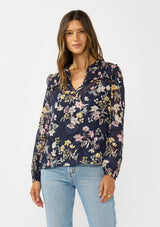 [Color: Navy/Yellow] A front facing image of a brunette model wearing a navy floral burnout blouse with smocked yoke, split v-neckline, and ruffle trims. 