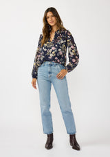 [Color: Navy/Yellow] A front facing image of a brunette model wearing a navy floral burnout blouse with smocked yoke, split v-neckline, and ruffle trims. 