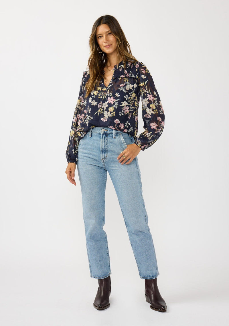 [Color: Navy/Yellow] A front facing image of a brunette model wearing a navy floral burnout blouse with smocked yoke, split v-neckline, and ruffle trims. 