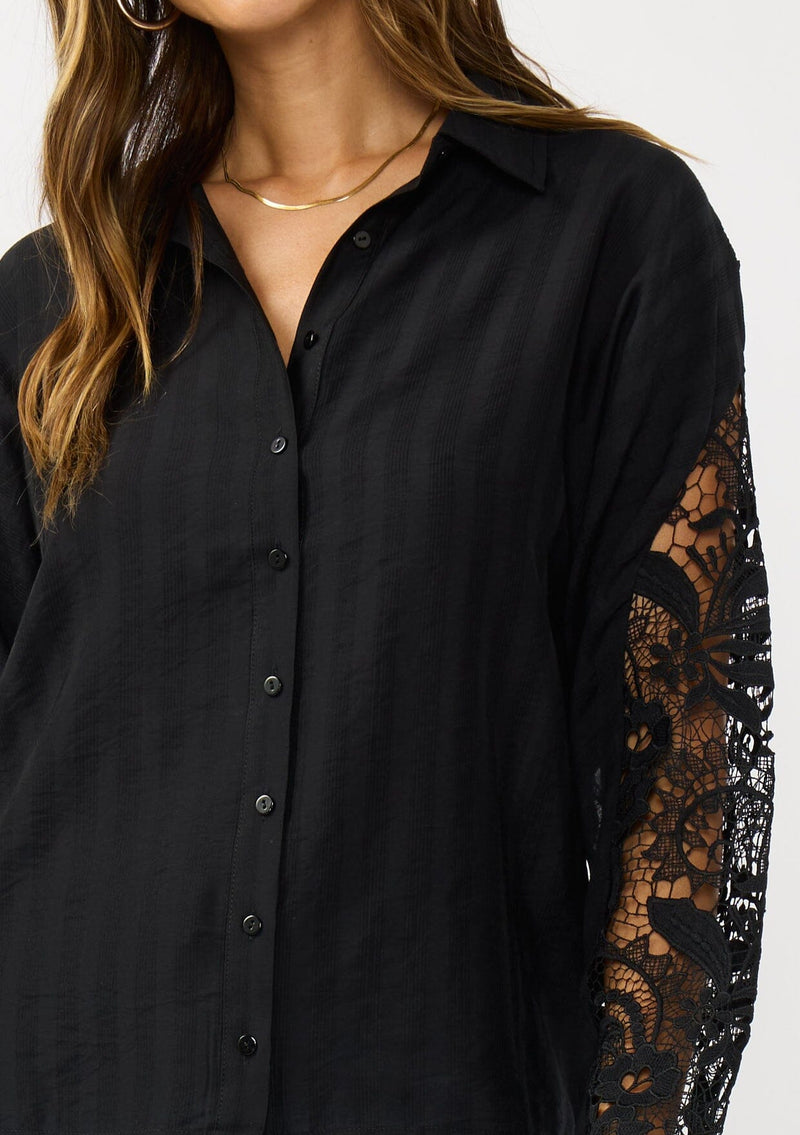 [Color: Black] A detail image of a blonde model wearing a striped jacquard black shirt with lace cutouts, a button front, and collared neckline. A cool and polished blouse for the fall season. 