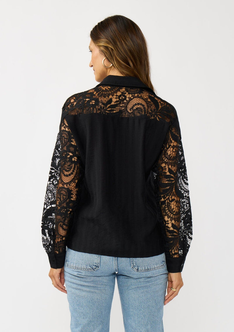 [Color: Black] A back facing image of a blonde model wearing a striped jacquard black shirt with lace cutouts, a button front, and collared neckline. A cool and polished blouse for the fall season. 