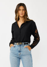 [Color: Black] A front facing image of a blonde model wearing a striped jacquard black shirt with lace cutouts, a button front, and collared neckline. A cool and polished blouse for the fall season. 