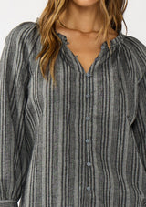 [Color: Charcoal] A detail image of a brunette model wearing a dark grey striped blouse with long sleeves, a split v-neckline, and button front. 