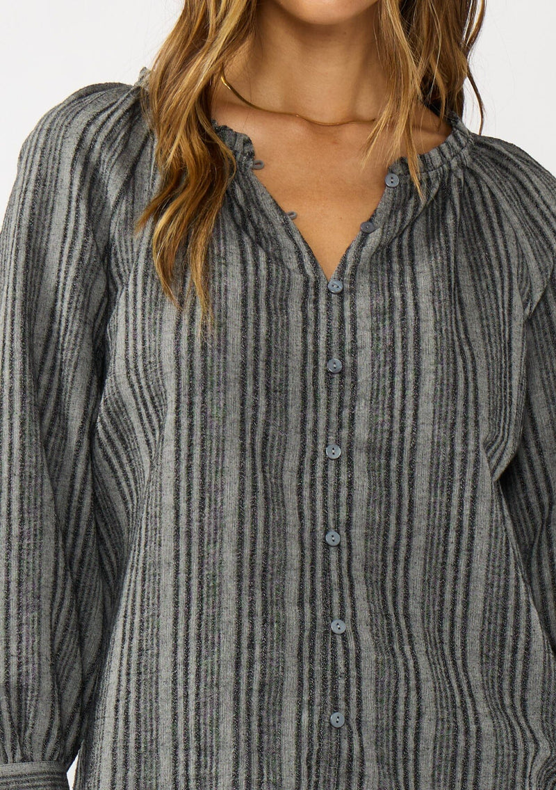 [Color: Charcoal] A detail image of a brunette model wearing a dark grey striped blouse with long sleeves, a split v-neckline, and button front. 