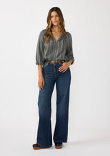 [Color: Charcoal] A front facing image of a brunette model wearing a dark grey striped blouse with long sleeves, a split v-neckline, and button front. 