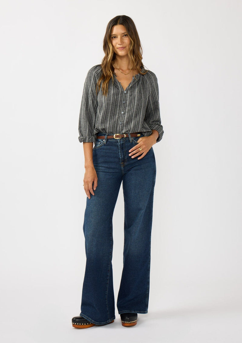 [Color: Charcoal] A front facing image of a brunette model wearing a dark grey striped blouse with long sleeves, a split v-neckline, and button front. 