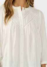 [Color: Cream/Black] A detail image of a brunette model wearing a boho striped button front blouse with a pintuck yoke, lattice trim, and voluminous sleeves. 